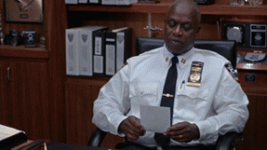 Captain Holt reading a piece of paper while sitting behind his desk